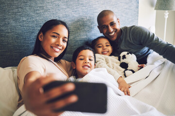 Poster - Parents, children or family selfie in a bed together with love, care and security or comfort. Woman, man and kids with a happy smile for quality time or profile picture in a home bedroom to relax