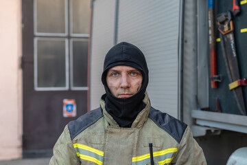 Wall Mural - Portrait of a tired firefighter in a protective suit standing by the fire engine after returning to the fire department