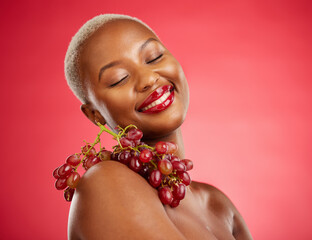 Poster - Skincare, smile and grapes with a model black woman in studio on a red background for health or nutrition. Beauty, happy and fruit with a young female person posing for wellness, diet or detox