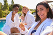 © Monkey Business - POV Shot Of Mature Female Friends Wearing Robes Outdoors On Loungers Drinking Champagne On Spa Day