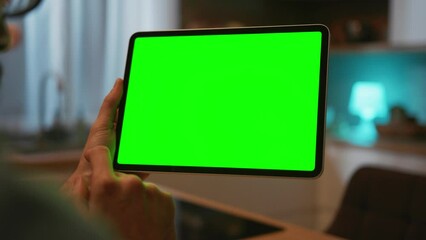 Adult young Caucasian person with beard sitting at table and using digital tablet with green screen. Man pointing with finger at digital tablet. Chroma key concept. Internet addiction. Gadget
