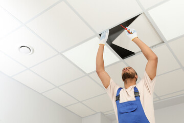 Electrician with screwdriver repairing ceiling light indoors, low angle view. Space for text