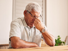 Stress, Headache And Old Man At Table In Home With Glasses, Worry And Fatigue In Retirement. Debt, Anxiety And Tired, Frustrated Senior Person With Mental Health Problem Or Crisis, Exhausted And Sad.