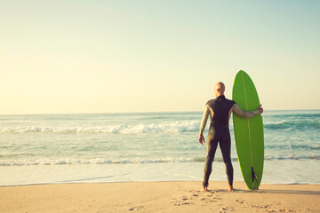 Wall Mural - Surfer on the beach holding is surfboaerd and watching the waves