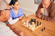© Theron/peopleimages.com - Retirement, playing and chess with senior men at nursing home for fun activity in home with nurse at table. Strategy, chessboard and challenge with elderly friends together on table for bonding.