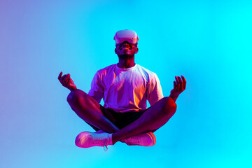 african american man meditates in virtual reality glasses and sits in the air in neon lighting