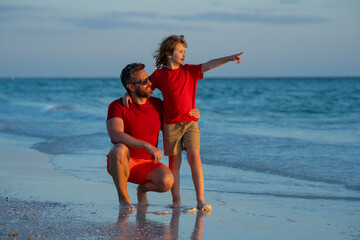 Wall Mural - Fathers day. Father walking with a little child son on beach near sea. Dad with son walking on a summer beach. Fathers love child. Father and son relaxing on sea. Summer holiday, vacation with father.