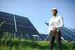 © Serhii - Portrait of Young indian man technician wearing white hard hat standing near solar panels against blue sky.Industrial worker solar system installation, renewable green energy generation concept.