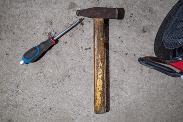 a screwdriver and a hammer on the concrete floor, next to an electric gun in the garage