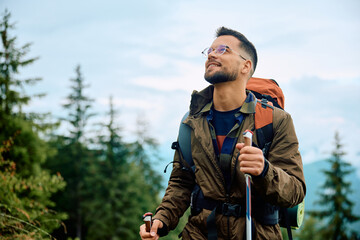 Happy backpacker using hiking pole while walking up hill.