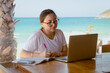 © aldo - young girl working and meeting at the beach wearing glasses and phones with a laptop