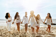 © Prostock-studio - Full length shot of happy ladies walking on the sea shore, holding hands and laughing, having hen party on the beach