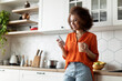 © Prostock-studio - Smiling Black Female Messaging On Smartphone And Drinking Coffee In Kitchen Interior