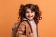 portrait of smiling schoolgirl with backpack looking at camera isolated on orange