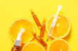 Ampoules with vitamin C, syringe, bottle of essential oil and orange slices on yellow background, closeup