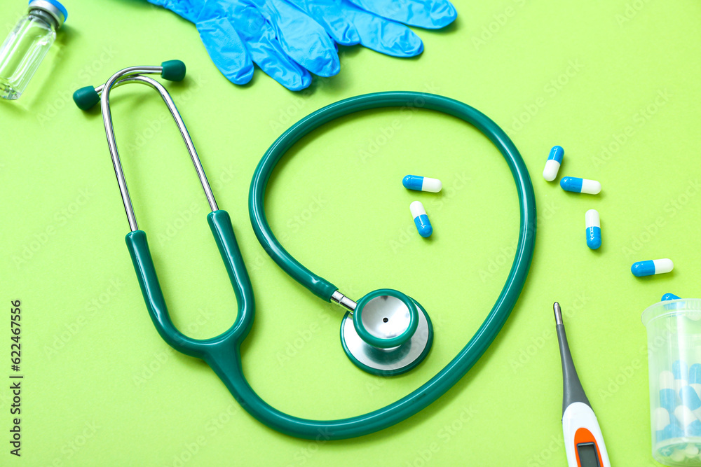 Stethoscope, medical gloves, thermometer and pills on green background
