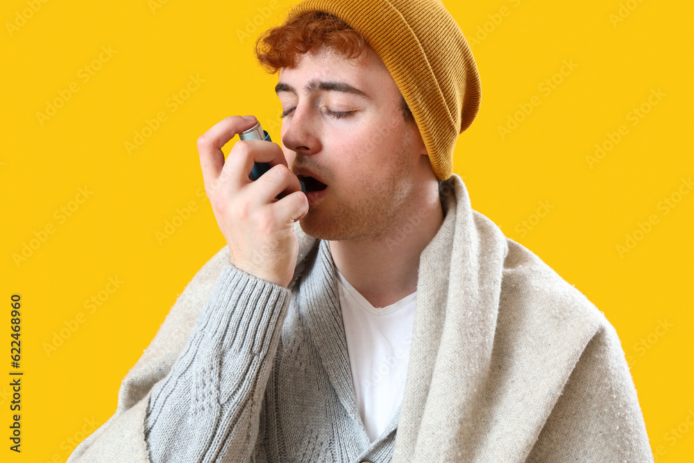Ill young man with inhaler on yellow background, closeup