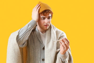 Wall Mural - Ill young man with thermometer on yellow background