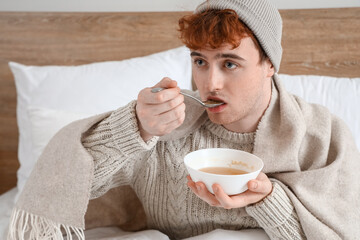 Wall Mural - Ill young man eating soup in bedroom