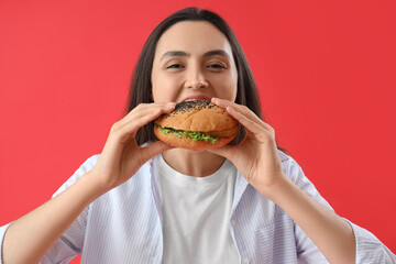 Young woman eating tasty burger on red background, closeup