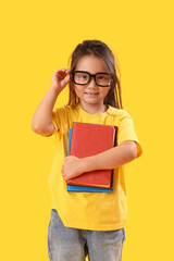 Poster - Little schoolgirl with books on yellow background