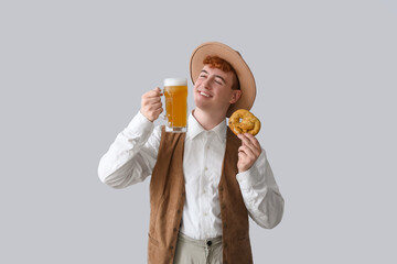 Young man in traditional German clothes with beer and pretzel on light background