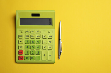 Calculator and pen on yellow background, flat lay with space for text
