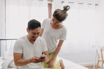 Wall Mural - Funny asian couple. Wife peeking husband who chatting on the smartphone.