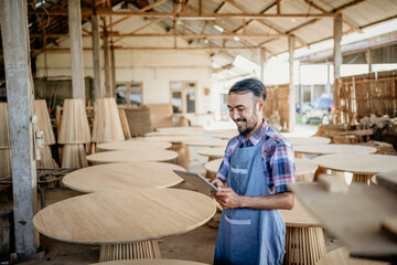 Wall Mural - Asian businessman using a tablet computer standing with wood craft shop in the background