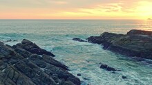 Aerial View Of A Slow Motion Scene Of Waves Hitting The Rocks At Bright Yellow Sunset..Waves Lapping On The Rocky Beach In The Bright Green Sea..The Green Sea Lapping On The Rocky Beach 