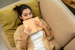 © Chanakon - Asian beautiful woman lay down on cozey couch sofa reading book in living room with sun light morning. People female stay home part time relax at home.