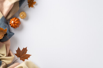 Enjoy the cozy autumn vibes at home: Top view photo featuring warming cashmere plaid, maple foliage and pumpkin candles on white backdrop. Ample space available for text or advertisements