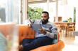 © Wavebreak Media - Focused african american man wearing jumper and using tablet on couch at home