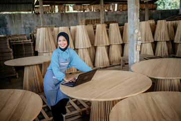 Wall Mural - Asian muslim women wearing hijab using laptop pc for working in traditional wood craft store