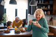 Happy carefree senior woman holding bowl with oatmeal muesli standing in the kitchen having breakfast at home.