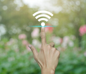 Hand pressing wi-fi flat icon over blur pink flower and tree in park, Technology internet communication concept