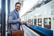© Dragana Gordic - Modern business travel demands modern technology. Handsome middle age businessman with suitcase standing in railroad station platform and waiting for high speed train or metro.