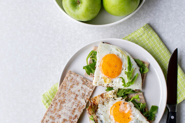 Wall Mural - Healthy breakfast with fried eggs, arugula, crispbread and green apple on a light background