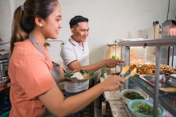 male customer choosing food with pointing finger and female waitress helping with food tongs at food stall display