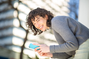 Wall Mural - Smiling young woman with cellphone standing outside in the city