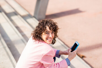 Wall Mural - Pretty woman with mobile phone looking behind sitting on steps outside