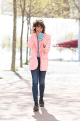 Wall Mural - Beautiful young woman with phone walking outside and smiling