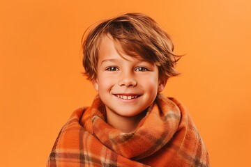 Wall Mural - Portrait of a smiling little boy wrapped in a blanket isolated over orange background