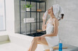 © VK Studio - Slim girl savors lotion scent, relaxes in home bathroom. Attractive European woman, towel-wrapped post-shower. Freshness, daily beauty routine.