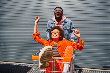 cheerful young african american best friends in sunglasses and bright outfits having fun with shoppi