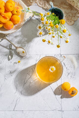 Chamomile tea, apricots and flowers on the light background close up. Top view