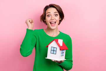 Sticker - Photo of shiny lucky girl dressed green sweater online holding small house rising fists isolated pink color background