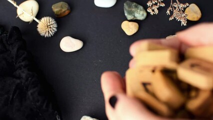 Wall Mural - Wooden runes pour out of the hands of a fortune teller on a black table with a velvet bag and stones. Magic esoteric symbols and signs for divination and prediction of the future and fate, top view.