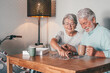 © luciano - Carefree senior couple at home spend time together doing a puzzle on the wooden table. Elderly man and woman enjoying free time in retirement