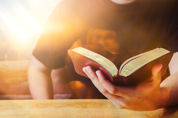 close up of a man hand holding the holy bible on wooden table against the sunlight with bokeh, chris